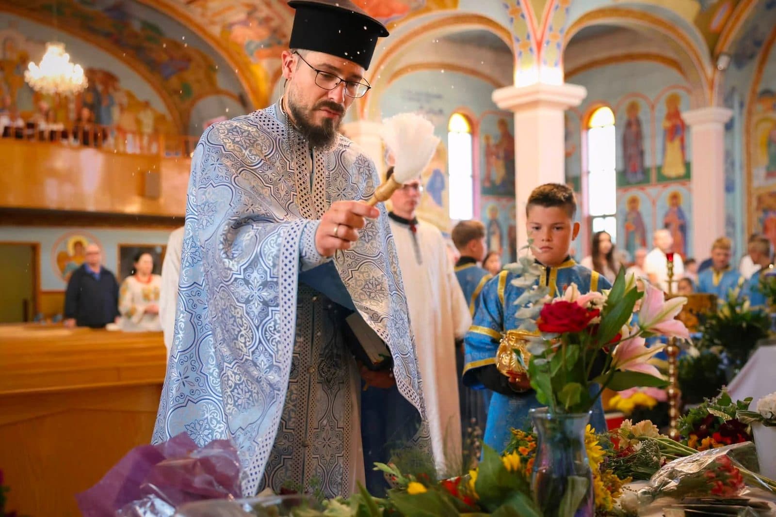 A priest carries incense through worshippers during a bright celebration inside the church.
