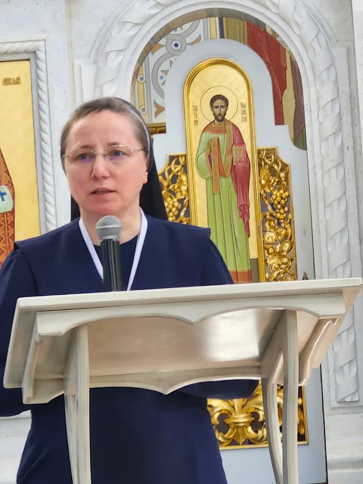 Sister speaks at a lectern in front of an iconostasis with an icon of Christ.