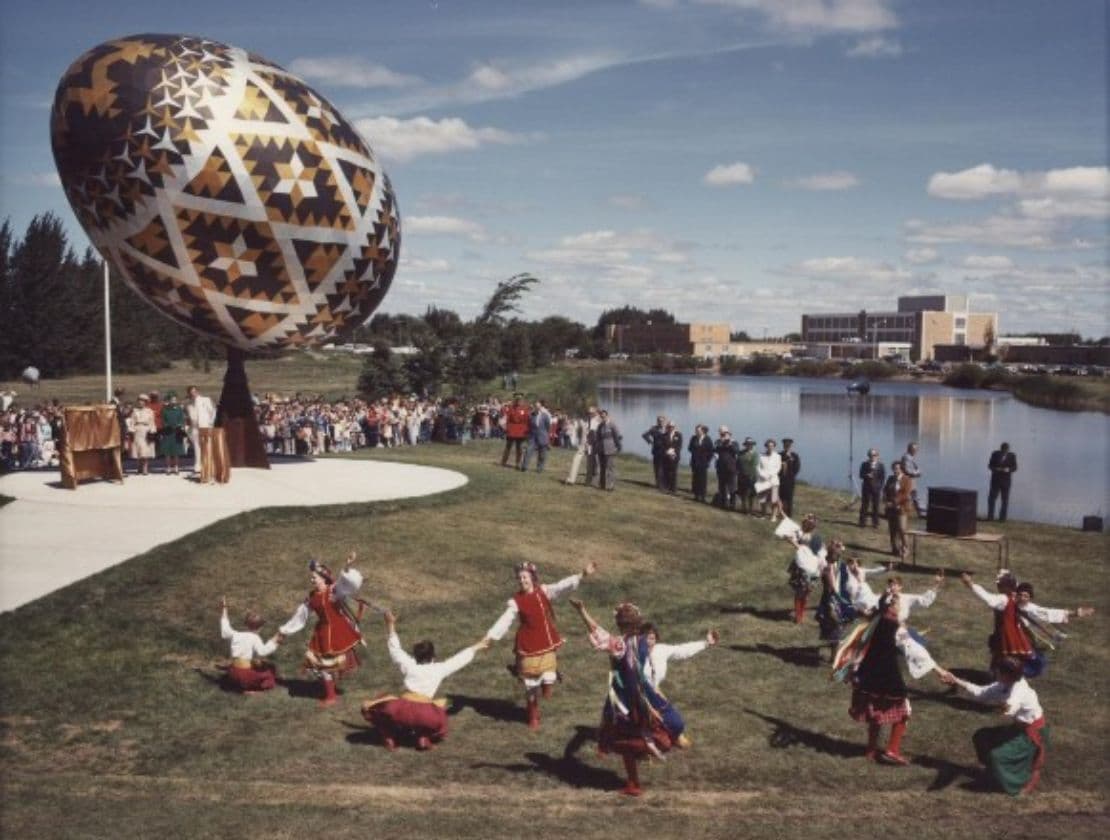 Giant pysanka sculpture unveiled with dancers and a crowd by a lake.
