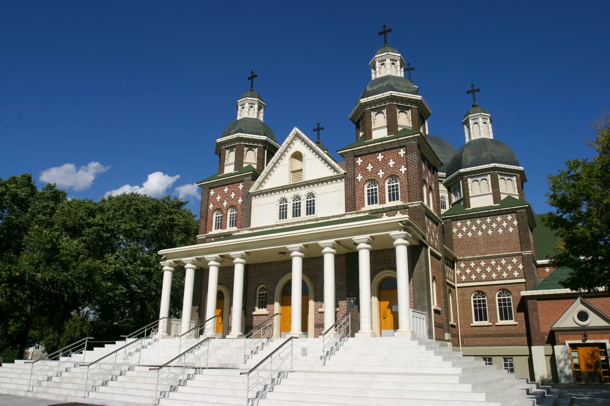 Brick church with multiple domes and a grand white staircase under a blue sky.