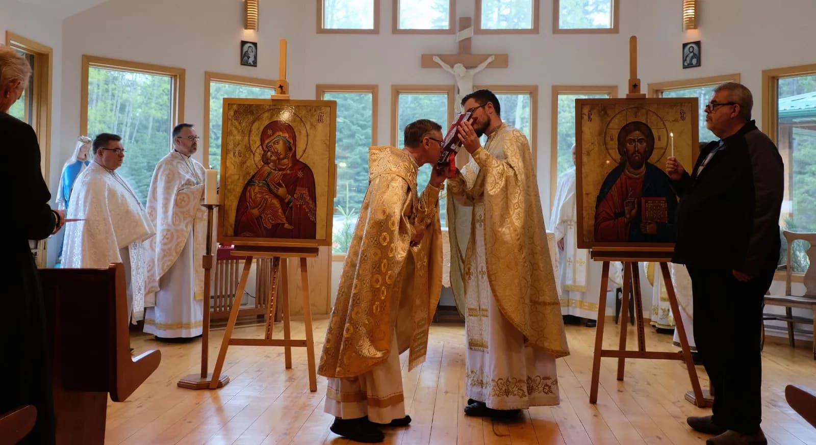Two priests in vestments kiss a book between two icons during a service.