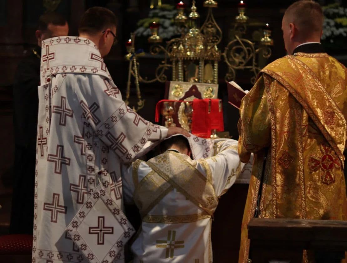 Priests in vestments perform a religious ceremony at an altar with a tabernacle.