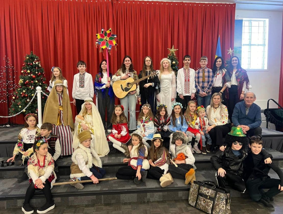 Children and adults in traditional Ukrainian clothing pose with a Christmas tree and a star.